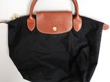 un sac à main noir muni d'une poignée marron, posé sur une surface blanche
