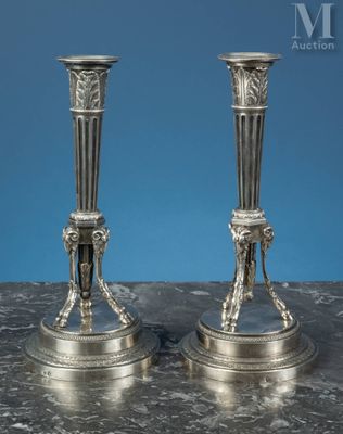 une paire de bougeoirs anciens en argent posés sur une table en marbre, sur fond bleu