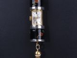 une horloge noire et dorée à laquelle est suspendu un pompon au bout de sa chaîne