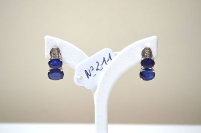 une paire de boucles d'oreilles en verre bleu et argent, posées sur un socle blanc