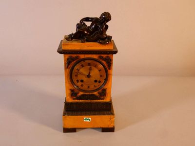 une petite horloge surmontée d'une statuette représentant un homme assis