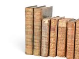 several old books are lined up in a row on a white surface