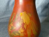 un vase rouge orné de motifs dorés, posé sur un tissu bleu