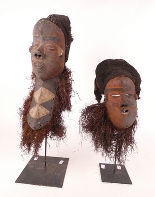 une paire de masques africains posés sur des socles, sur fond blanc