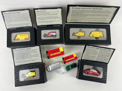 Plusieurs petites voitures miniatures se trouvent dans une boîte noire posée sur une surface blanche.