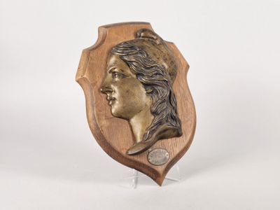 an image of a bronze plaque of a woman ' s head on a wooden stand
