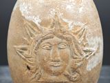 un pot en terre cuite orné d'un visage, posé sur une table