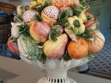 un vase blanc rempli de fruits et de légumes posé sur une table