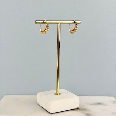 une paire de boucles d'oreilles créoles en or posées sur un socle en marbre