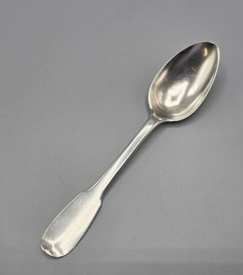 une cuillère en argent à long manche posée sur une surface grise
