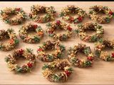 Des couronnes de Noël sont disposées sur une table en bois, accompagnées de pommes de pin