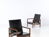 a pair of black leather lounge chairs in the style of person