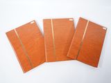 trois cahiers marron posés sur une surface blanche, sur fond blanc