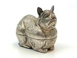 une figurine en argent représentant un chat assis sur une surface blanche