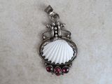 a close up of a silver pendant with a shell and garnets on it