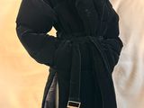 Le manteau est noir et comporte une boucle dorée au niveau du col.