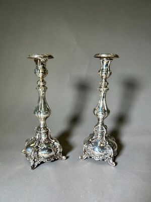 une paire de bougeoirs en argent posés sur une table, sur fond gris