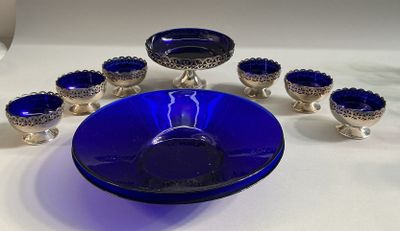 a blue glass bowl and six silver cups on a table