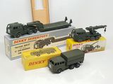 trois véhicules militaires miniatures et une pile de boîtes posés sur une surface blanche