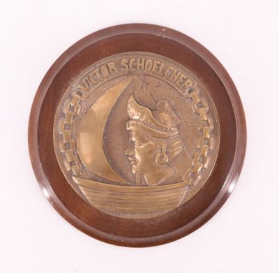 une médaille d'or sur laquelle est représenté un voilier, sur un fond blanc
