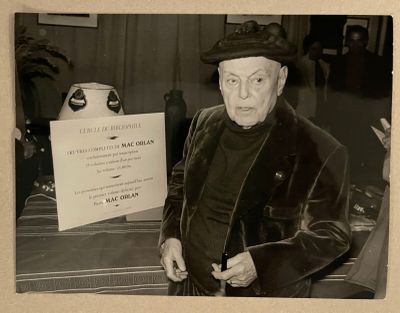 photographie en noir et blanc d'un homme portant un chapeau et un manteau, tenant une pancarte