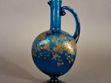 a blue and gold vase with a handle on a table