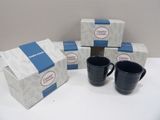 three black coffee mugs sitting on a table next to a box