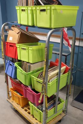 Des bacs aux couleurs vives sont empilés sur un chariot métallique dans une pièce