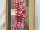 tableau représentant une fleur rose dans un cadre doré, posé sur un tissu blanc