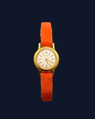 une image représentant une montre en or avec un bracelet rouge sur fond bleu