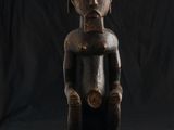 une vieille statue en bois représentant un homme assis sur un fond noir