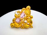 une photo d'une bague en or sertie de pierres roses, posée sur une assiette blanche