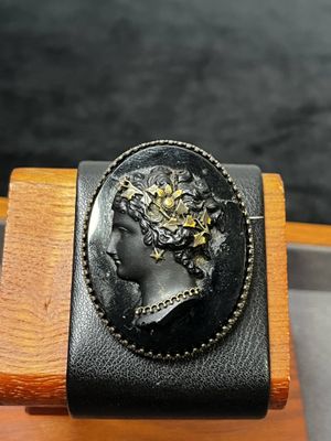 une image représentant une broche noire et dorée orné d'un visage de femme