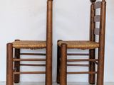 pair of antique wooden chairs with woven seats against a white wall