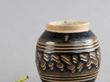 un petit vase noir muni d'un couvercle en bois, avec une figurine verte à côté