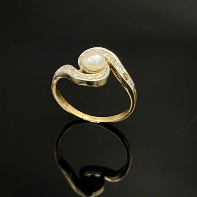 un gros plan d'une bague en or sertie d'une perle, posée sur une surface noire