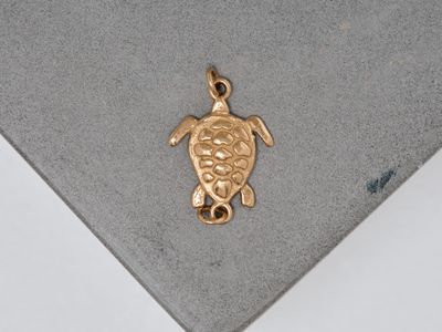 gold plated sea turtle charm on a grey surface