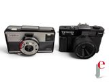 two cameras sitting next to each other on a white surface
