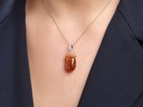 a close up of a woman wearing a necklace with an orange stone