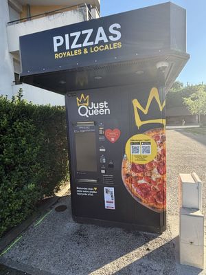 un distributeur automatique sur lequel est posée une pizza, devant un immeuble