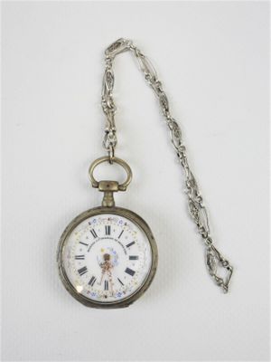 une montre de poche en argent avec une chaîne, posée sur une surface blanche