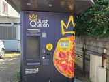 un distributeur automatique sur lequel est posée une pizza, devant un immeuble