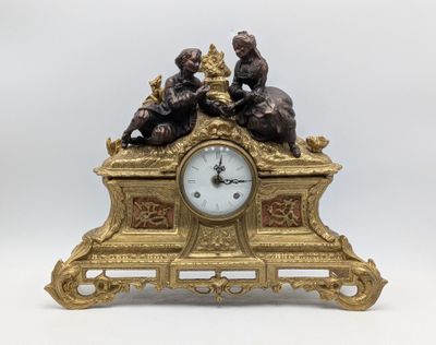 a gold clock with a statue of a boy and a girl on it