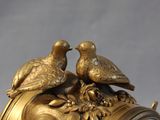 a gold clock with two birds on top of it