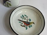 a small plate with a bird on it next to a tea pot