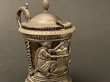 a silver vase sitting on a table with a bird on it