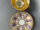 two gold cups and saucers with purple and white designs on them