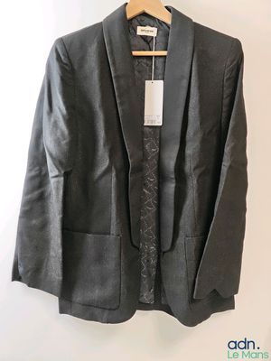 un blazer noir orné de dentelle, suspendu à un cintre sur un mur blanc