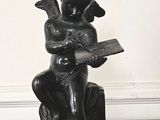 une statue représentant un garçon assis sur un rocher, en train de lire un livre
