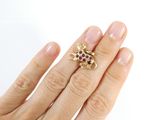 a woman ' s hand holding a gold ring with red stones
